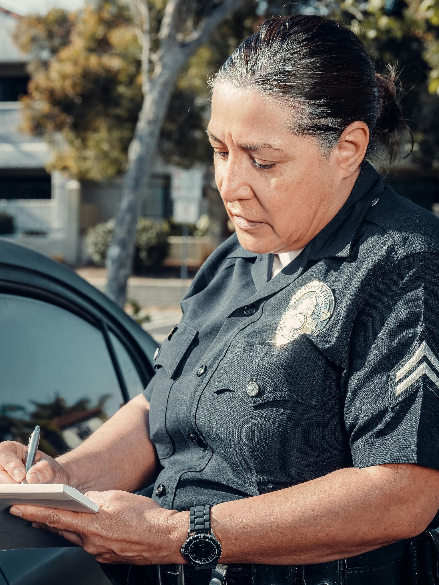 Photograph of a policewoman writing a ticket with a vehicle in the background.