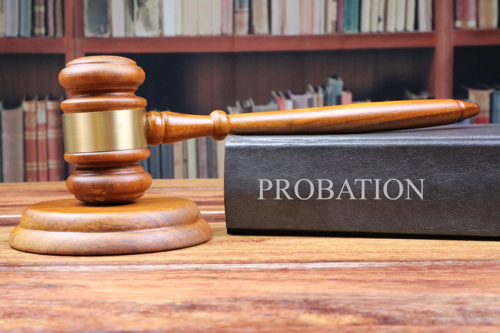 Image showing a wooden gavel resting on a black book entitled, “Probation” with shelves of books in the background.