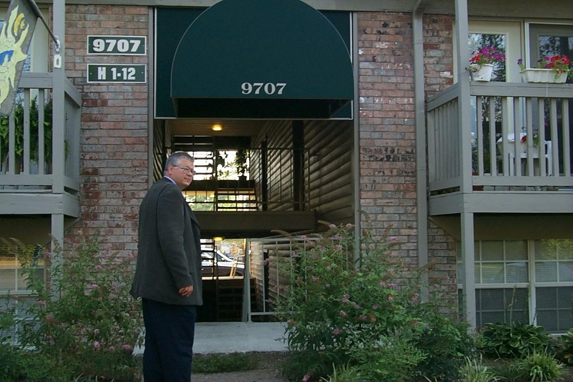 Photograph showing a well-dressed communities corrections officer standing outside an apartment building.