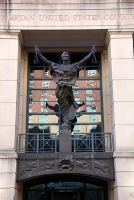 Close-up image of Albert V. Bryan United States Courthouse in Alexandria, VA, featuring a prominent bronze statue of Lady Justice at the center of the main entrance.