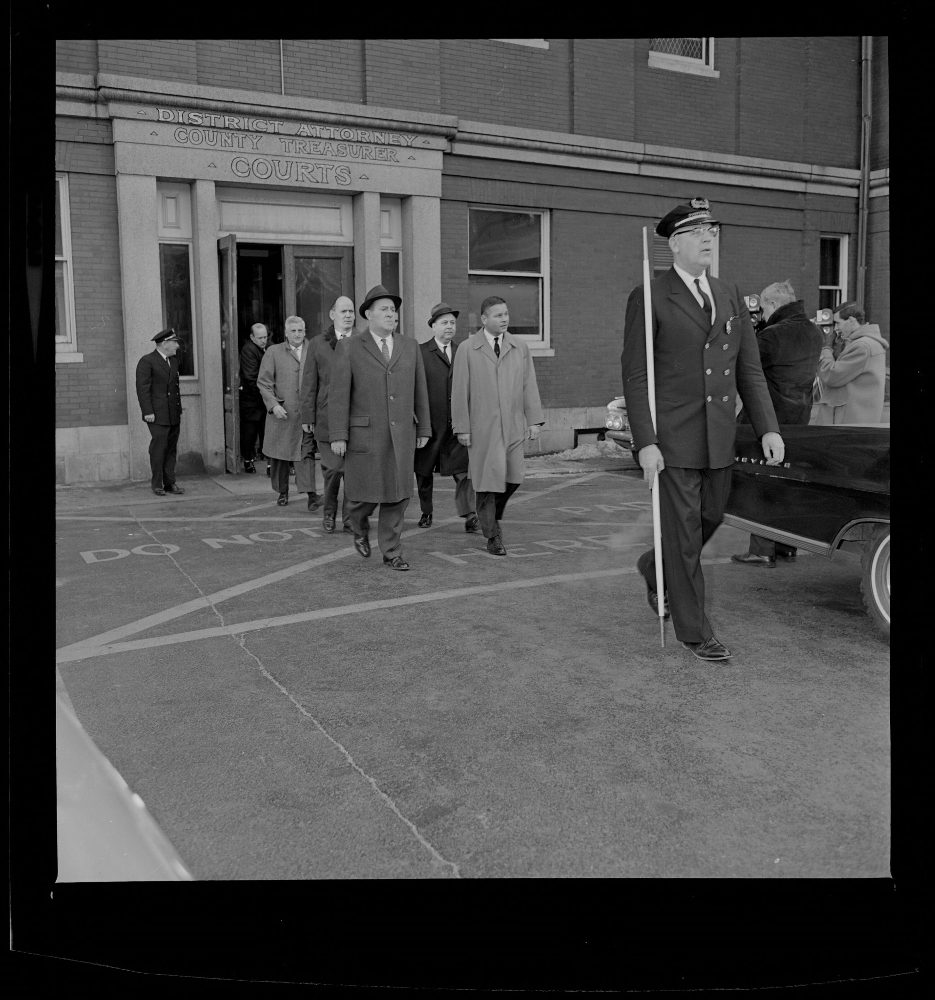 Photograph showing several solemn male jurors exiting the courthouse, escorted by the bailiff.