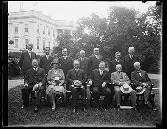 Photograph of President Herbert Hoover with the twelve members of the Wickersham Commission on the North Lawn, the White House in the background.