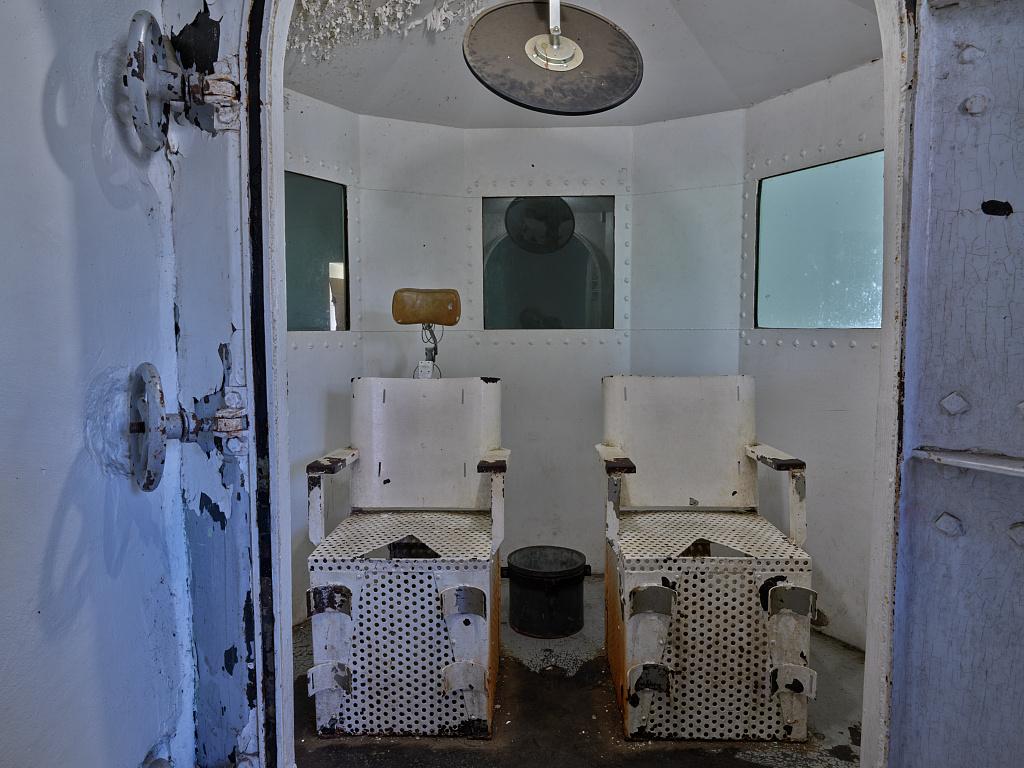 Photograph of a dilapidated gas chamber with two seats.