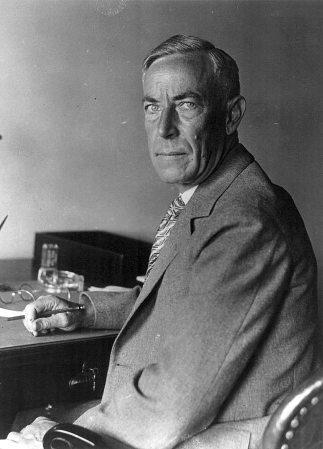 Photograph of August Vollmer, appearing professional, seated at a desk with a pen in hand.