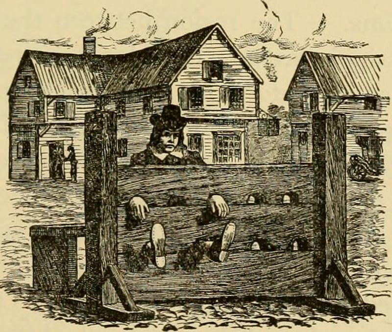 Ink illustration depicting a man dressed in Puritan attire, with his hands and feet firmly bound in substantial wooden stocks, positioned prominently in the heart of a Colonial American village.