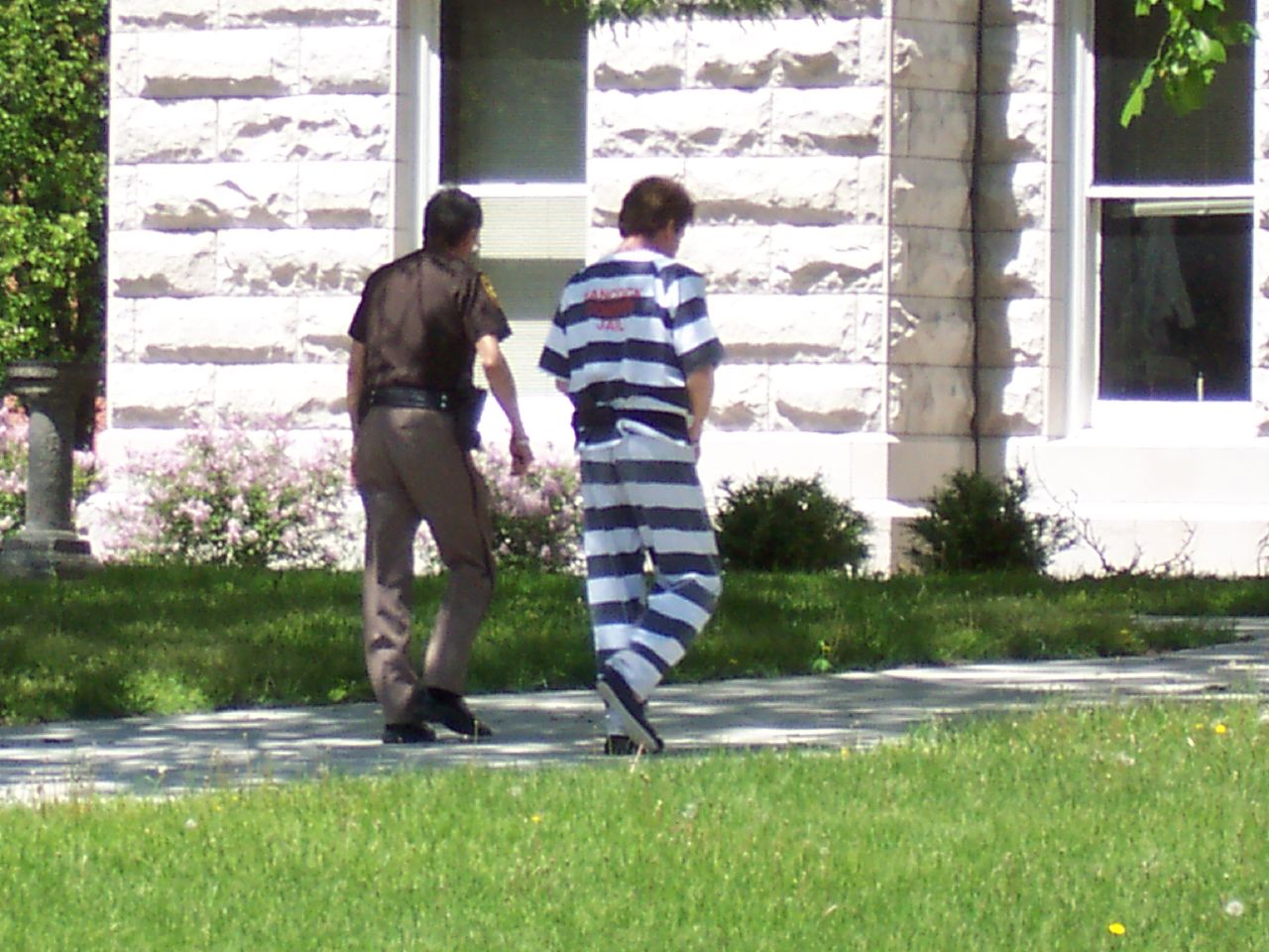 Photograph showing a jail inmate walking with a correctional officer into a building.