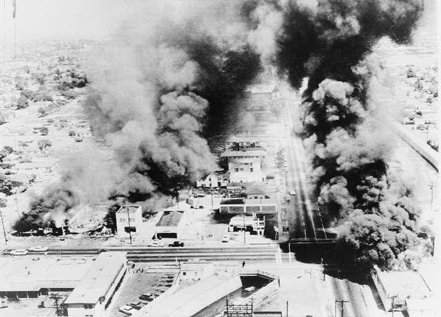 Photograph showing an aerial view capturing multiple burning buildings emitting thick plumes of black smoke during the 1965 Watts Rebellion in Watts, California.