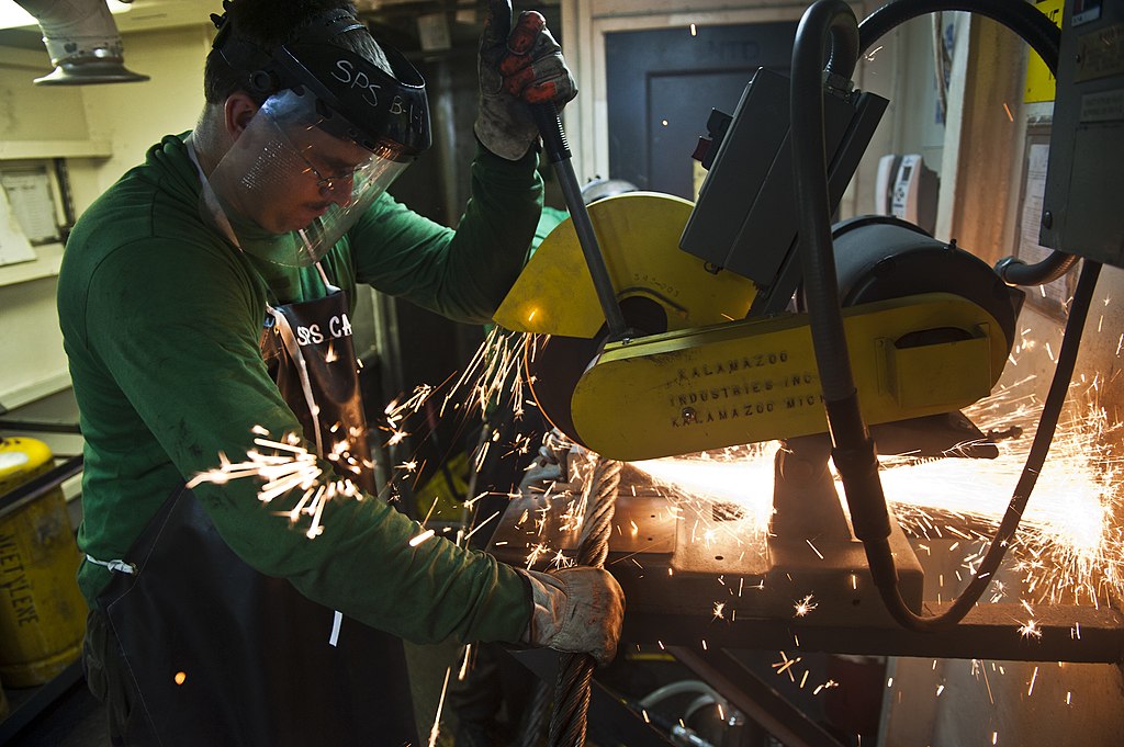 Abrasive saw cutting material, creating sparks. Person holding saw.