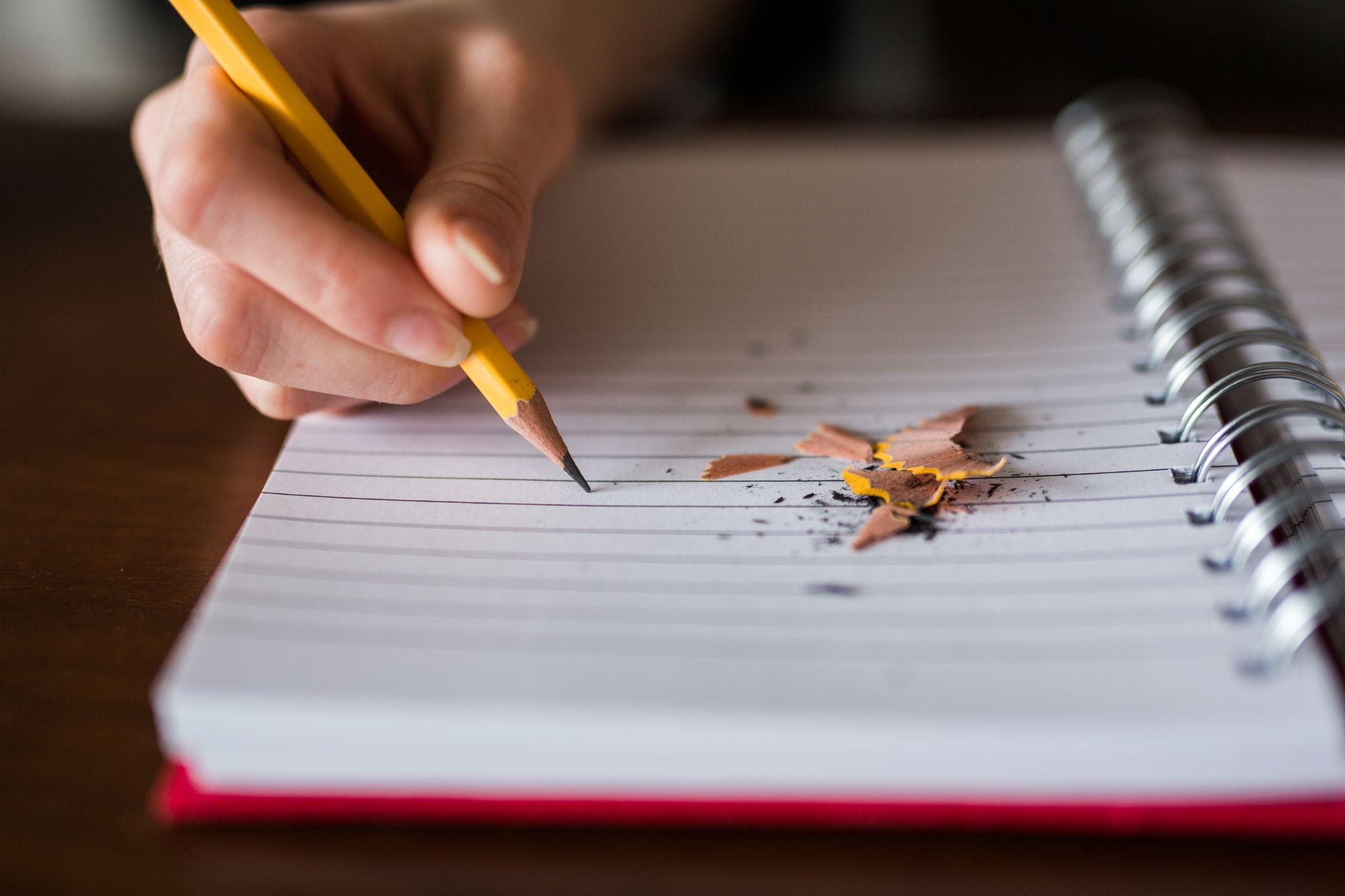 Pencil poised above a paper notebook with pencil shavings on the page.