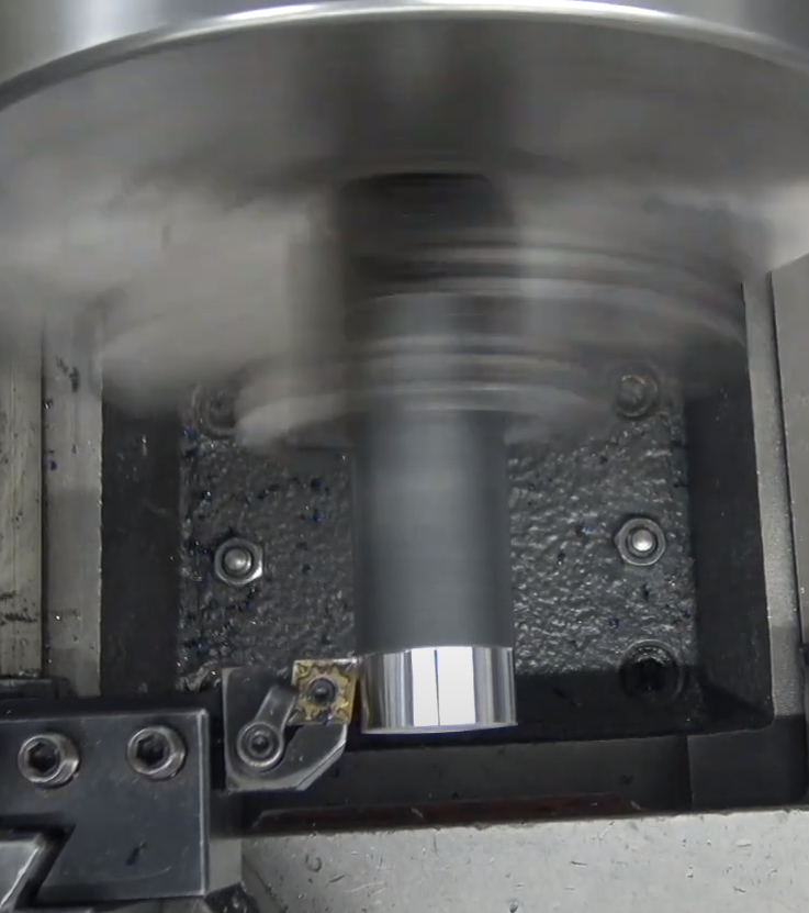 A piece of round bar stock is being held in a rotating chuck while a turning tool removes material.