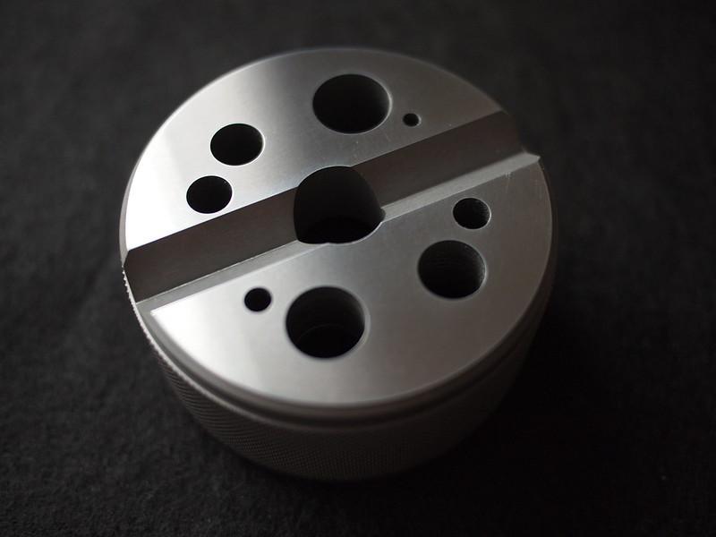 Picture of a circular steel block. A groove down the middle, with holes randomly in a circular pattern.