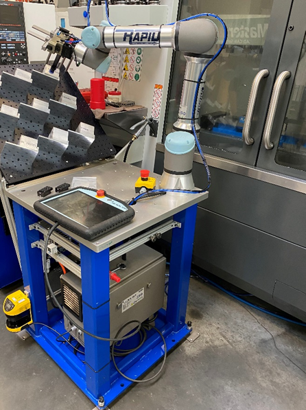 A Universal Cobot stands outside the closed doors of a CNC mill waiting for the machine to finish machining a part so it can change out the part with a new piece of stock.