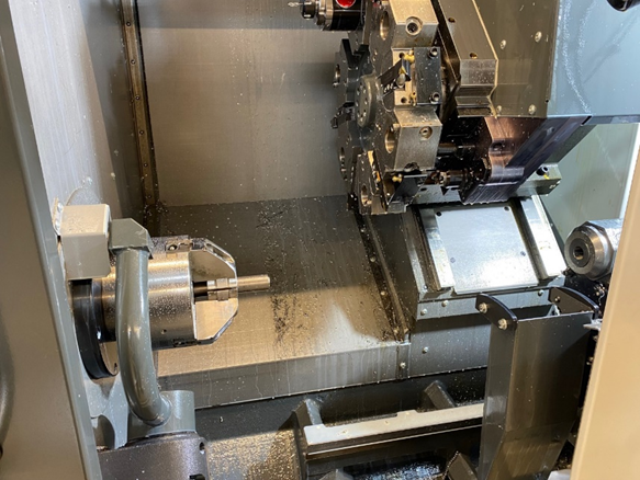 A view of the work area inside a CNC lathe. The spindle on the left has a piece of steel bar in the chuck, and the tooling turret near the top has all the cutting tools installed.