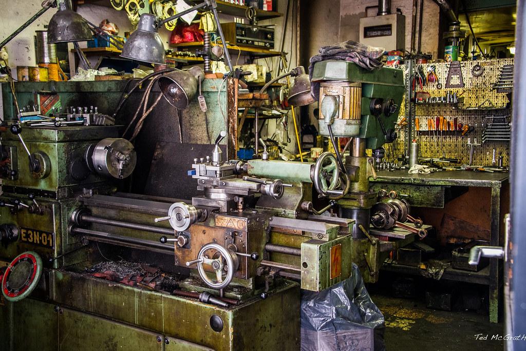 An old and dirty machine shop cluttered with necessary tooling for lathe operation.