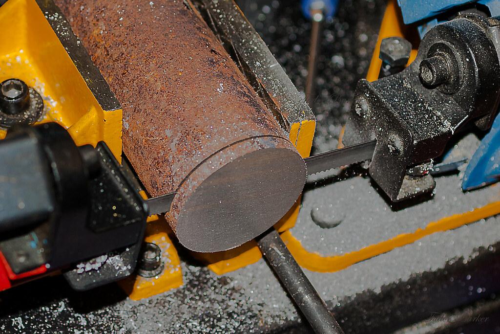 A three inch round steel bar being cut on a band saw.