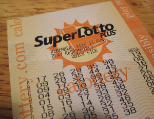 An orange paper lottery ticket with six columns of random numbers. At the top of the ticket are the words “Super Lotto Plus”.