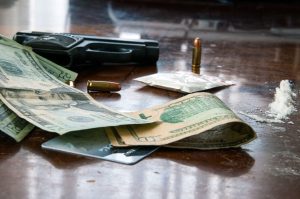 Close-up photo of cash, drugs, bullets, and a handgun on a wooden table.