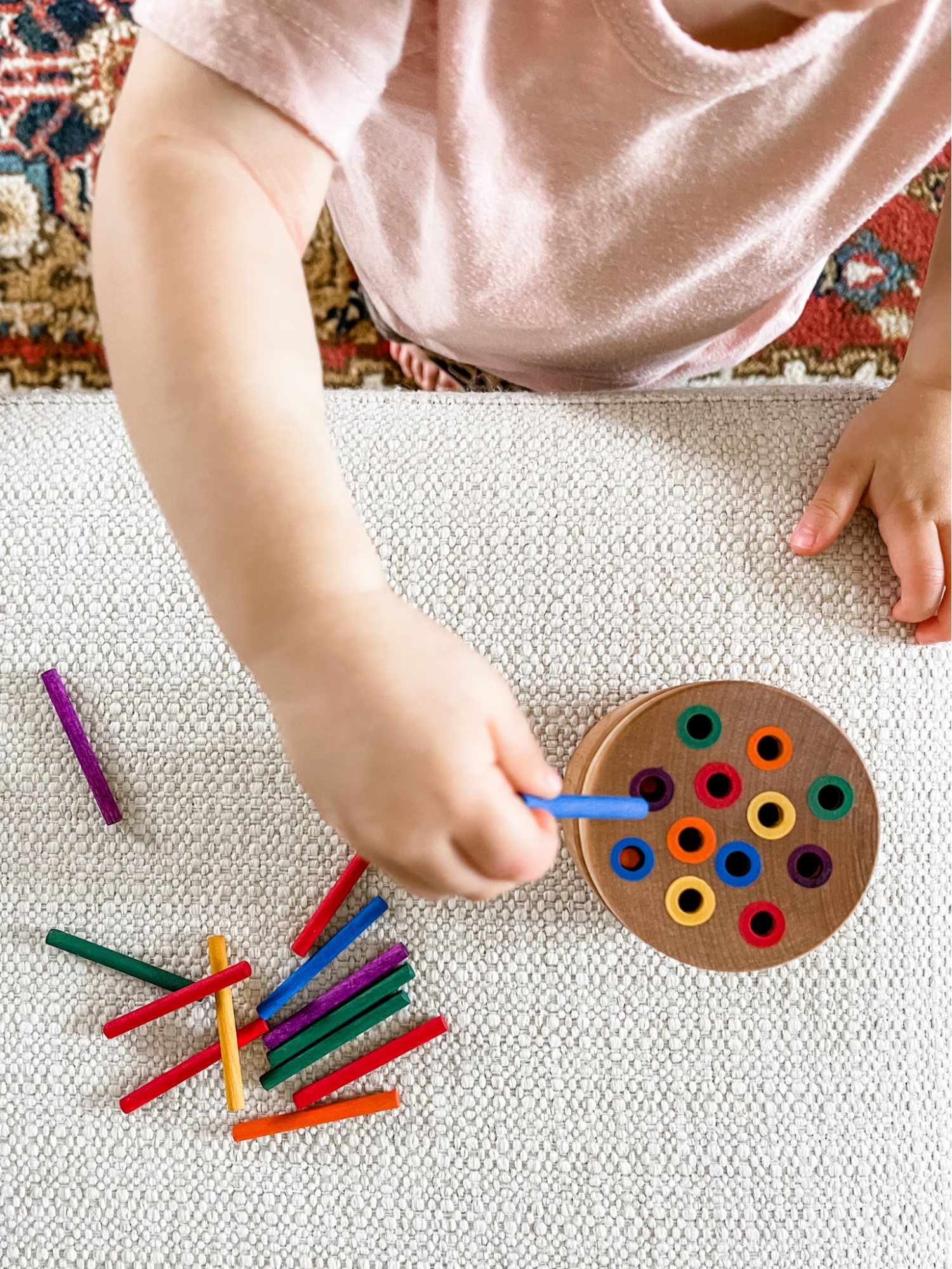 Child using a Montessori material that has colored sticks which are placed into colored holes.