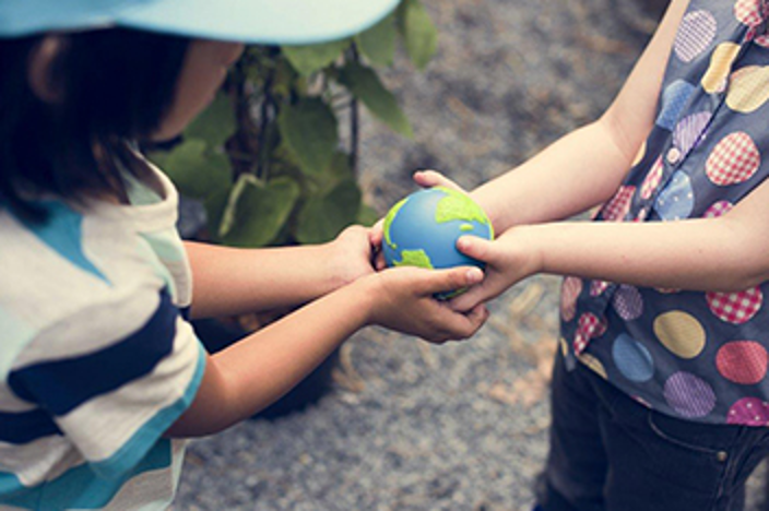 Two children jointly hold onto a single Earth globe.