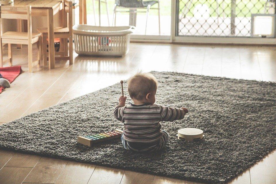 A toddler playing with a xylophone and a drum on a living room rug.