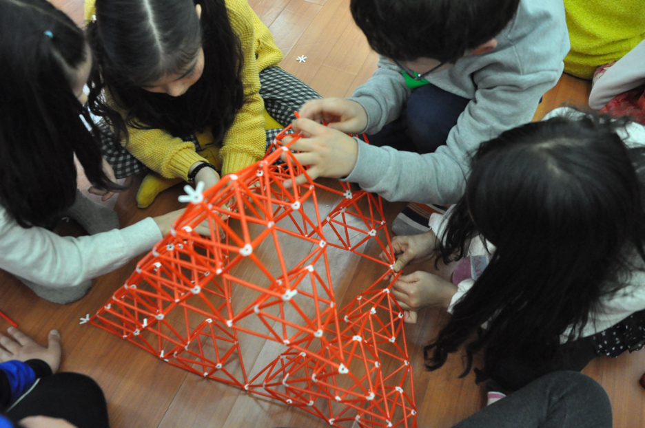 Four children put together a construction toy pyramid with commercially made toy straw.