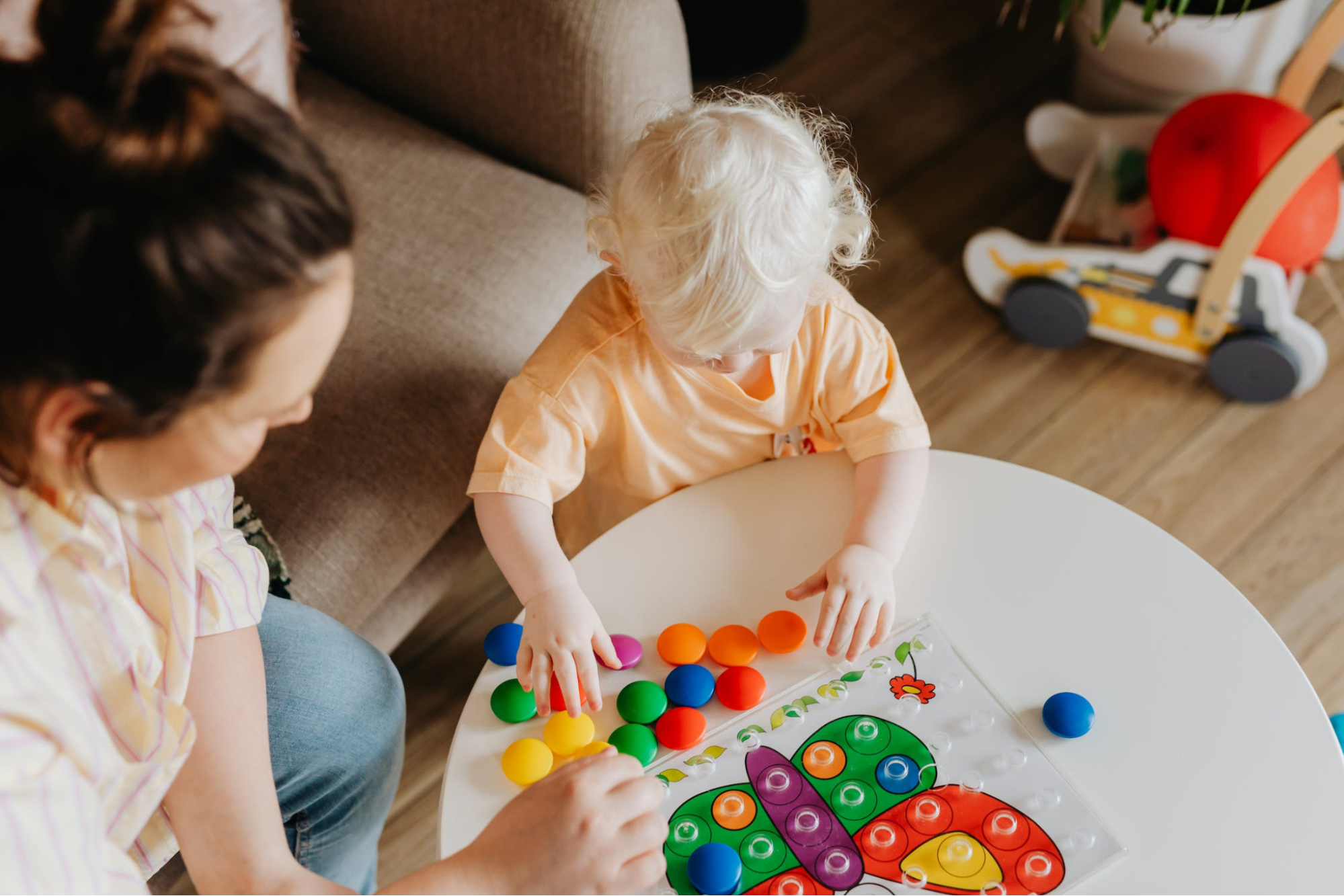 Child reaching for a colored peg, adult reaching for colored peg, a toy with colored holes to fit pegs into.