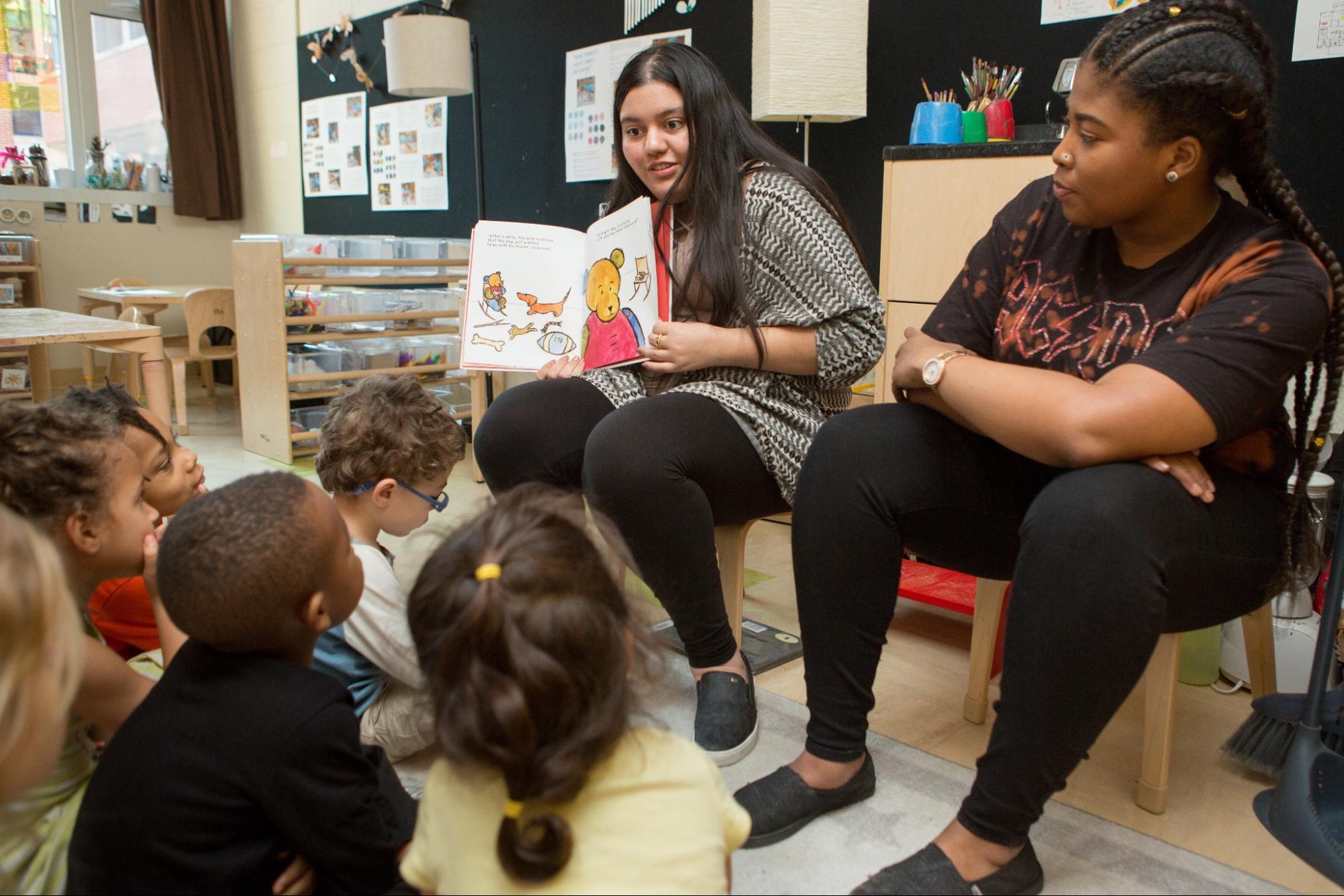 Teachers sitting with children in circle time and reading a book.