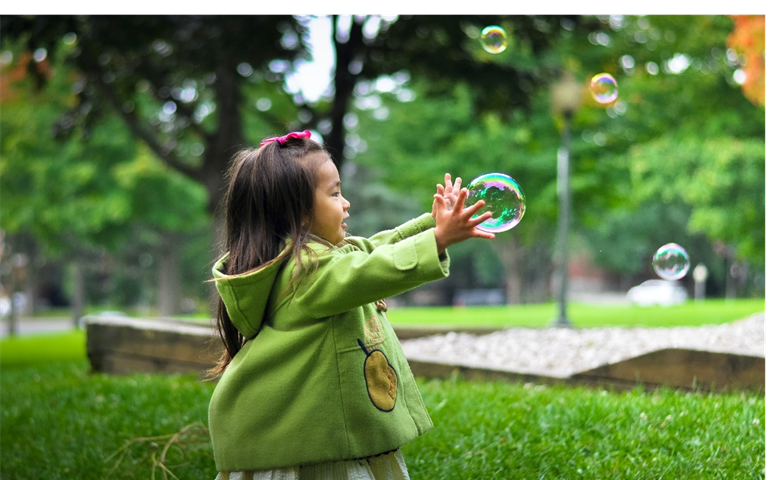 Child with arms extended toward a soap bubble