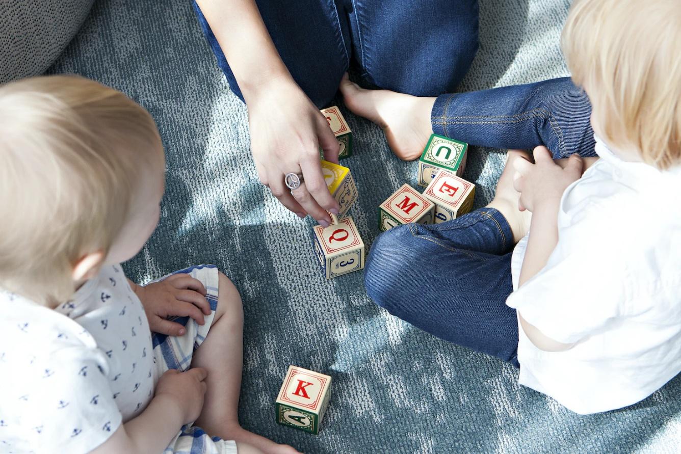 Mom with 2 children on floor with letter blocks. Mom engages with the play to support learning for the children.