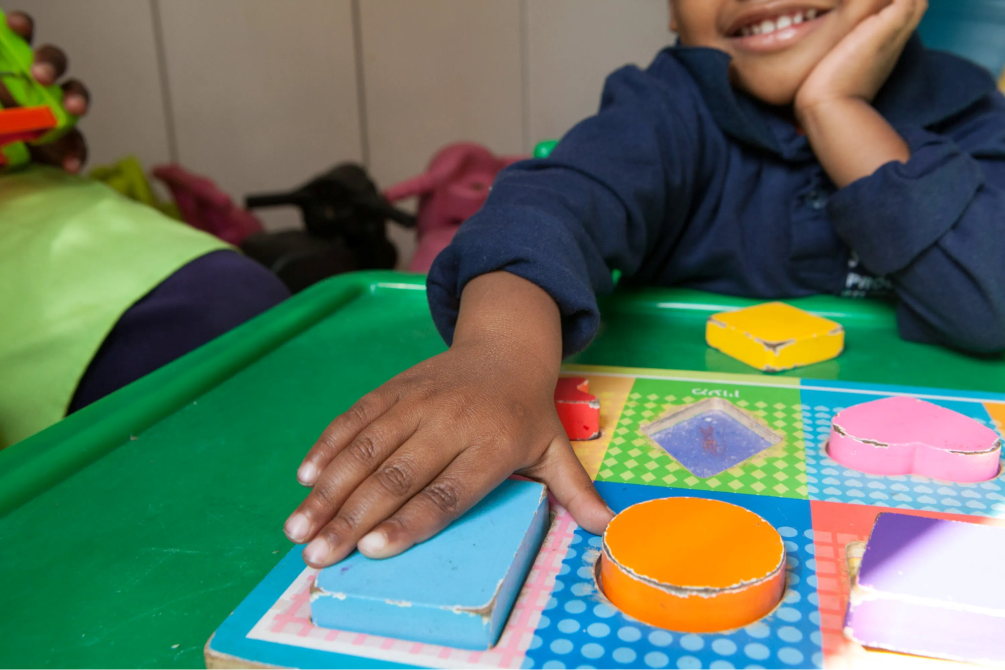 Child places a rectangular puzzle piece on a puzzle board.