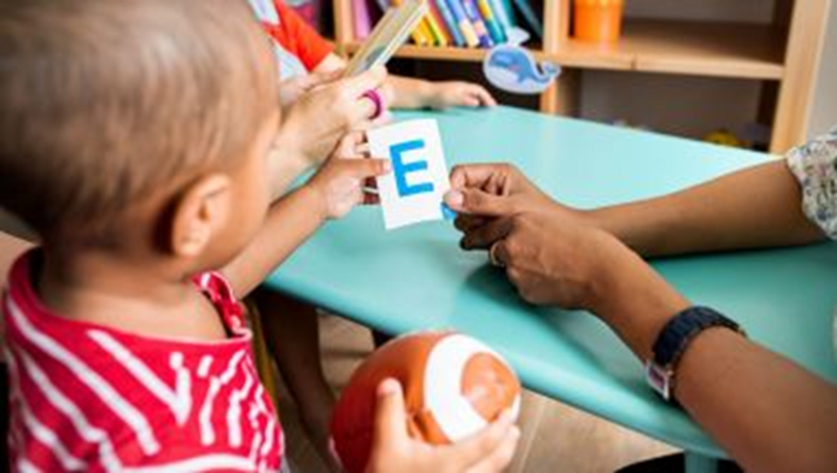 A young child holds a card with the capital letter E on the left edge while an adult holds the right edge.