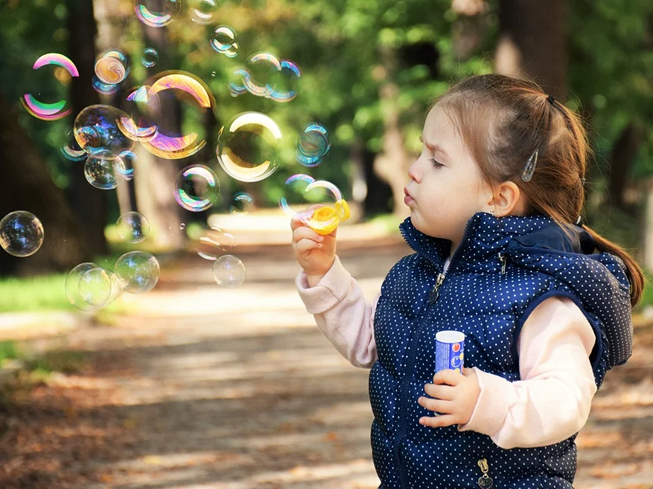 Young girl outside blowing bubbles. Photo indicates an aspect of positive behavior.