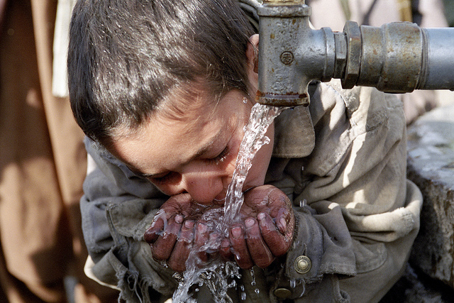 A child drinking water from a faucet