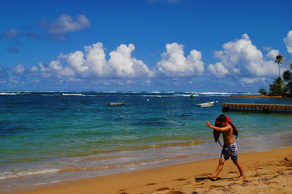 Boy walks along beach carrying a lifejacket.