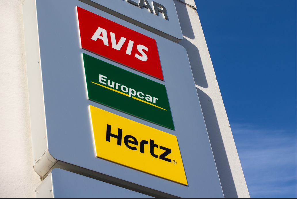 Sign shows three car rental companies: Avis, Europcar, and Hertz.