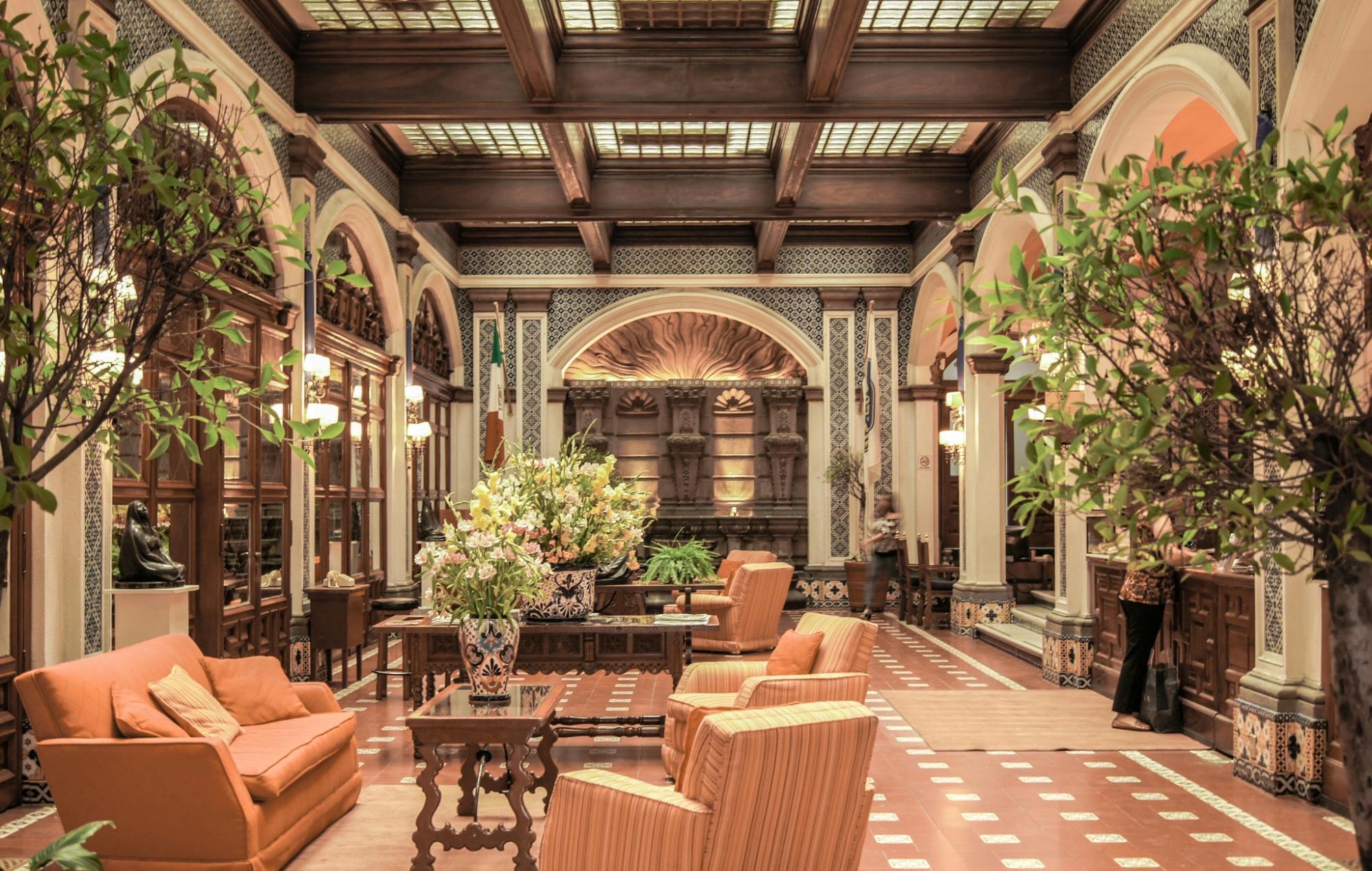 Interior of a luxury hotel lobby featuring arches, wood beamed ceilings, orange sofas and potted plants.