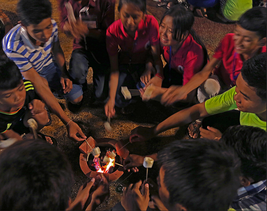 Cambodian exchange students prepare s’mores around a nighttime campfire.