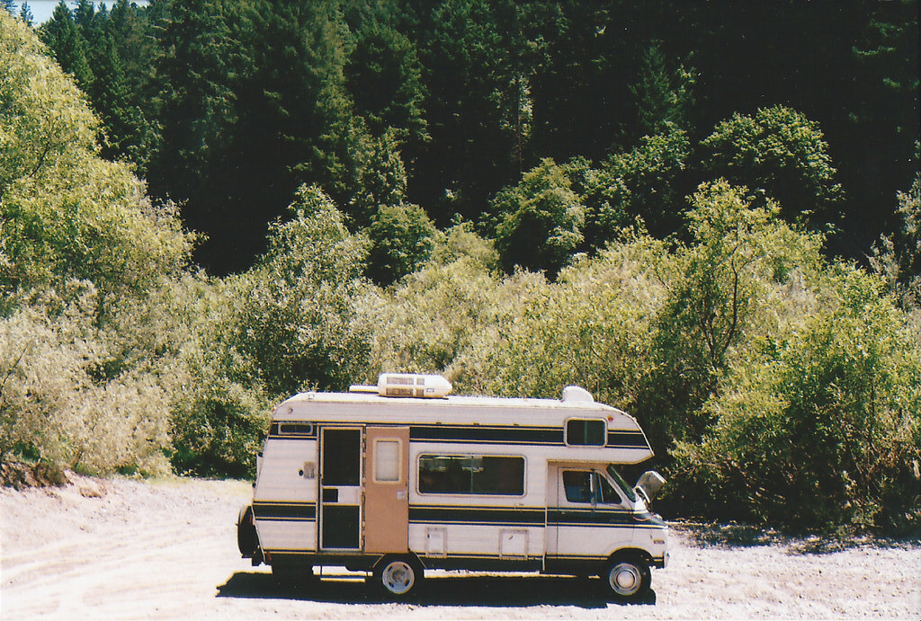 A recreational vehicle drives to a campsite with trees in the background.