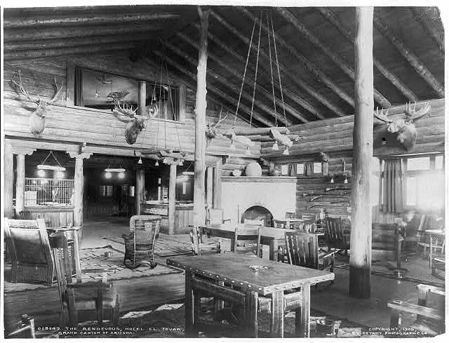 Black and white photo of a hotel lounge, built as a log cabin, with various decorations including moose and elk heads along the walls.