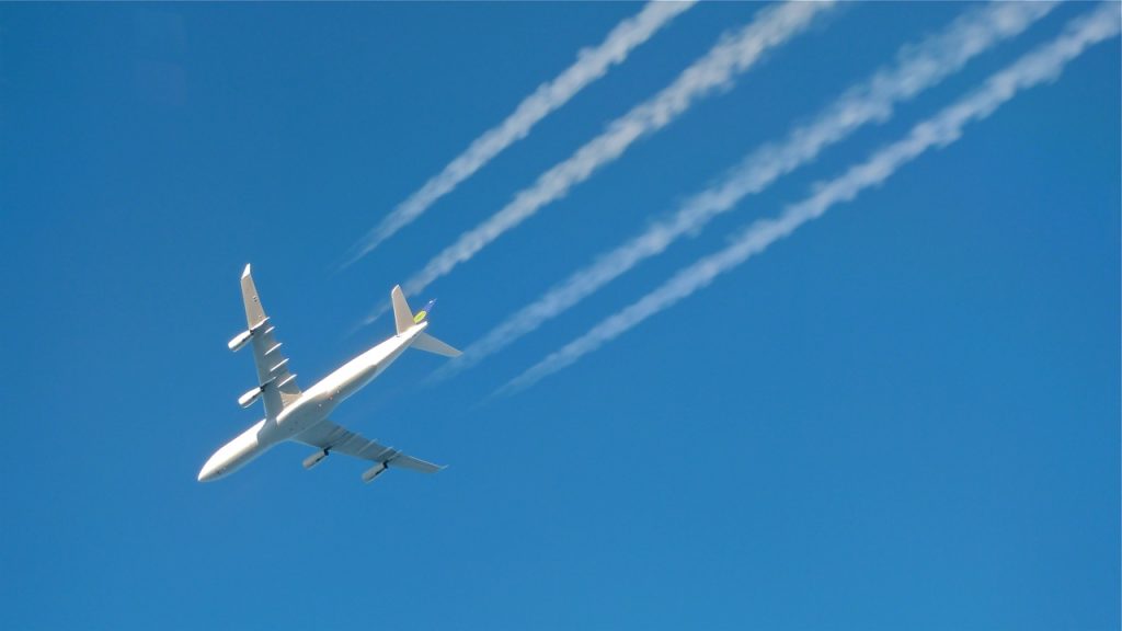 A white passenger plane leaves contrails behind in a bright blue sky.