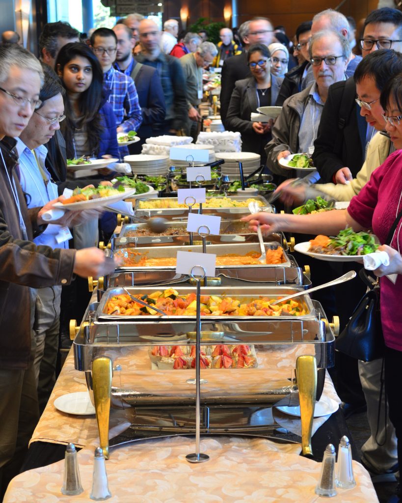 Two lines of people in business attire move down either side of a catered buffet.