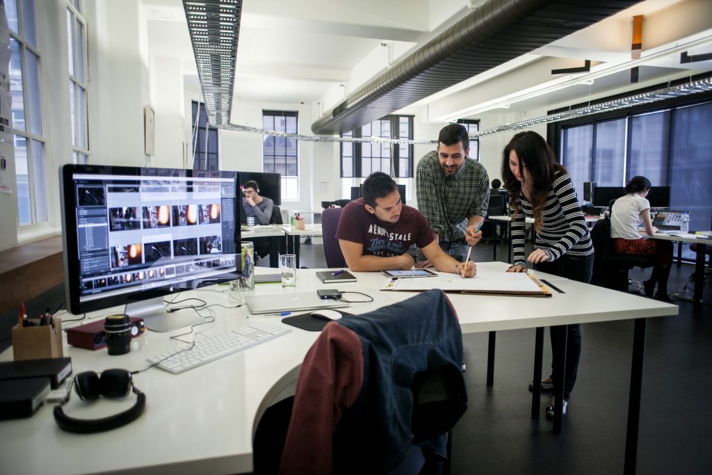 Several people stand around a work desk, sketching something on a large notepad.