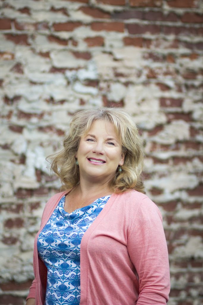 A woman in a blue and white top smiles at the camera against a brick backdrop.
