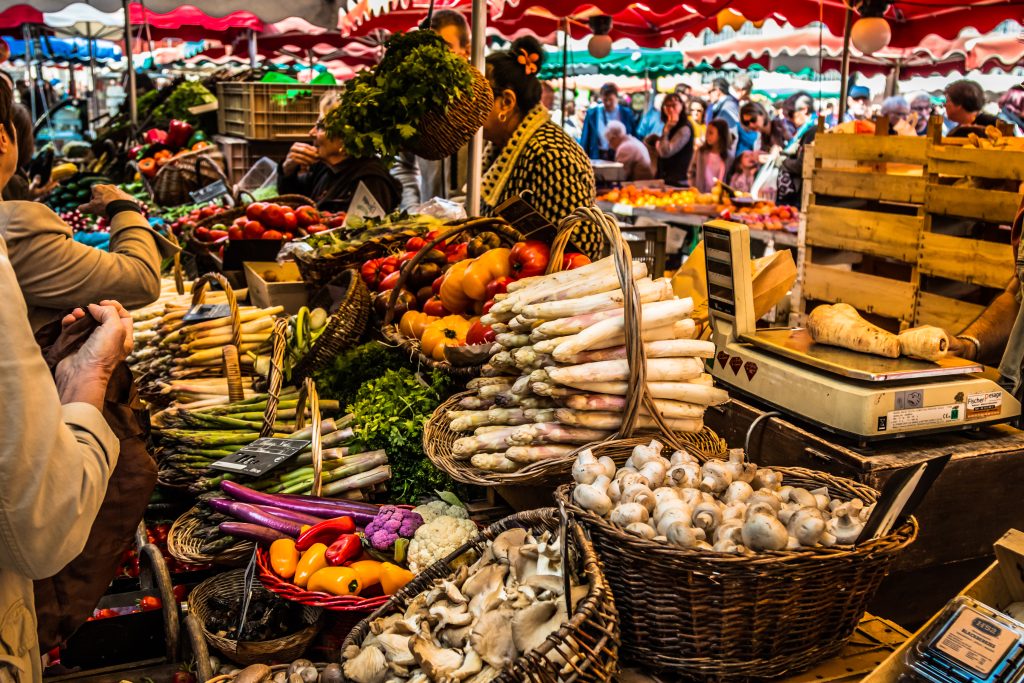 A colorful array of fresh produce is laid out in wicker baskets at a busy open-air market.