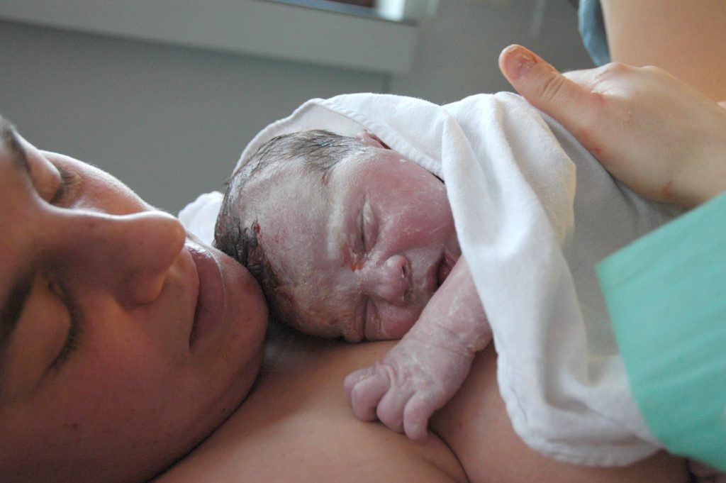 Image showing a Baby on mother's belly right after birth, skin covered in vernix and some blood