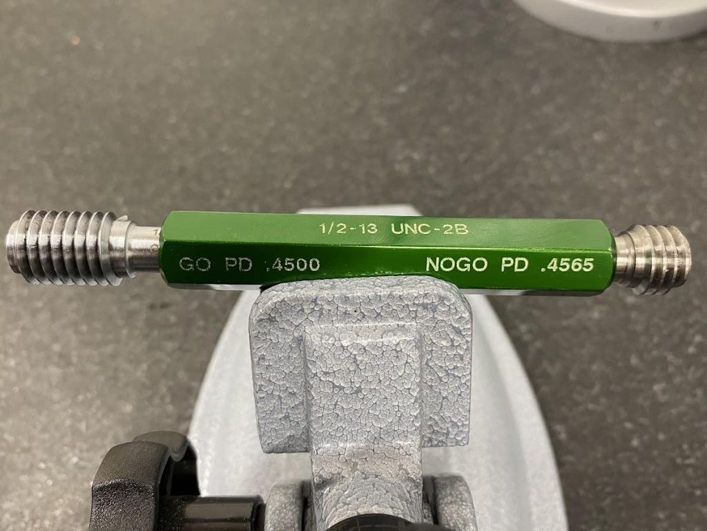 A close up view of a ½-13 UNC 2B thread gage with an end marked “GO” and the other marked “NOGO”.