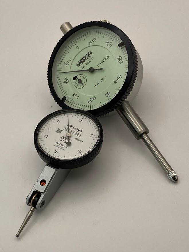 A dial indicator and a smaller test indicator sitting on a surface.