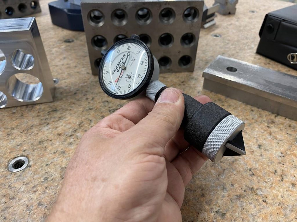 An operator is holding a chamfer gage which has a pointed plunger and a dial indicator.