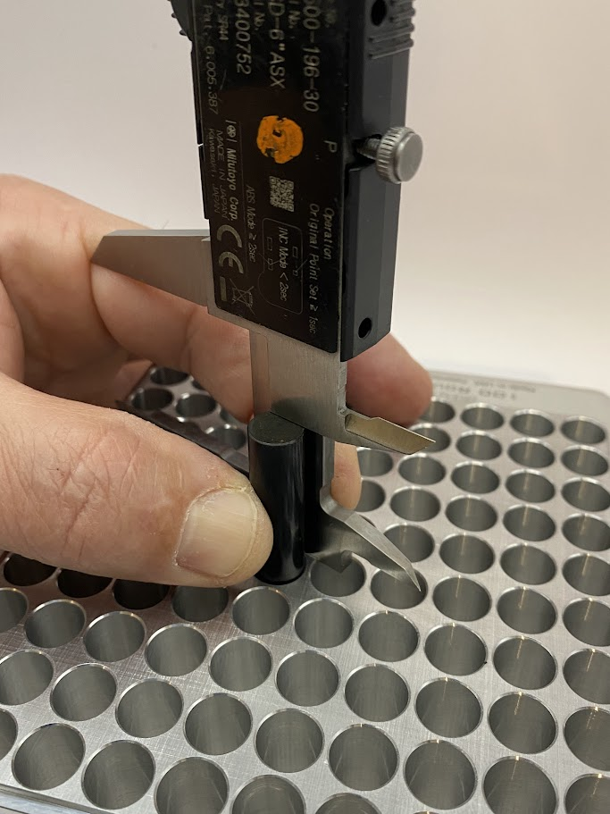 The operator's fingers are holding the caliper against the pin while maintaining contact with the surface of the part.