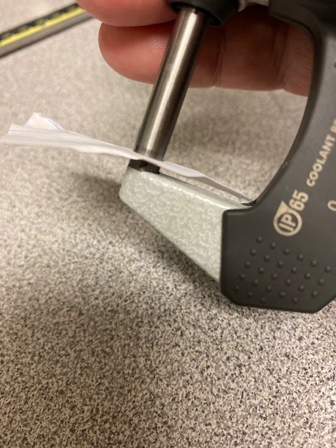 The spindle is closed onto a slip of paper on a zero to one inch micrometer.